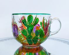 a glass coffee cup with colorful cactus designs on the inside is sitting on a reflective surface