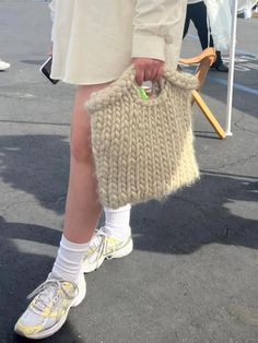 a person wearing white shoes and holding a knitted handbag in their right leg