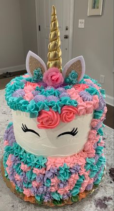 a cake decorated with pink, blue and green icing has a unicorn's face on it