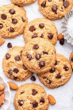 chocolate chip cookies with almonds and pecans scattered around them on a white surface