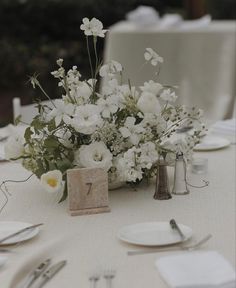 the table is set with white flowers and silverware