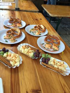 several plates with pretzels, cheese and fruit on them sitting on a wooden table