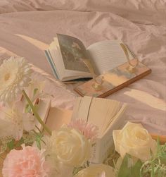 an open book sitting on top of a bed next to pink and white flowers in a vase