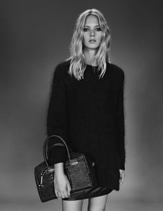 a woman holding a handbag and posing for a black and white photo with her legs crossed