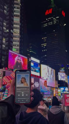 a person holding up a cell phone in the middle of a busy city at night