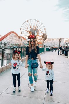 a woman and two children wearing minnie mouse ears walking down a sidewalk in front of a ferris wheel