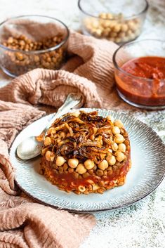 a white plate topped with food next to bowls of sauce and nuts on a table