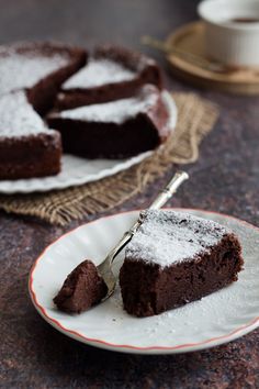 a slice of chocolate cake with powdered sugar on top and a fork in the foreground