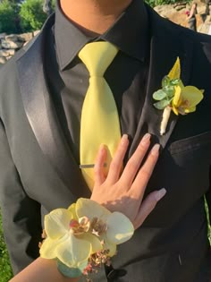 a man in a suit and yellow tie is holding a boutonniere with orchids on it