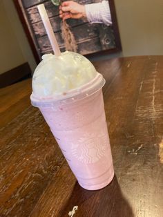 a pink drink sitting on top of a wooden table next to a framed photo with a hand holding a straw