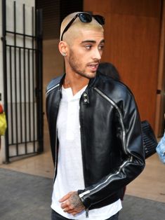 a man with a shaved head wearing a black leather jacket and white t - shirt