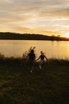 two people holding hands while walking by the water at sunset or sunrise with clouds in the sky