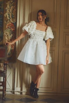 a woman in a short white dress leaning against a wall