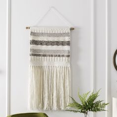 a white wall hanging on the side of a room next to a green chair and potted plant