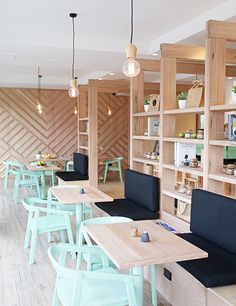 an empty restaurant with blue chairs and wooden shelves on the wall, in front of a wood floor