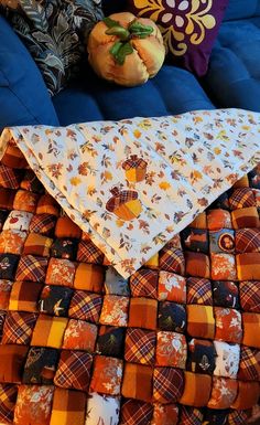 an orange and brown blanket sitting on top of a blue couch next to two pumpkins