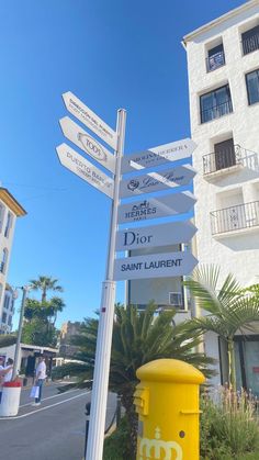 a yellow post with many signs on it in front of a white building and palm trees