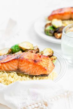 salmon and vegetables on couscous with water in the bowl next to plated food