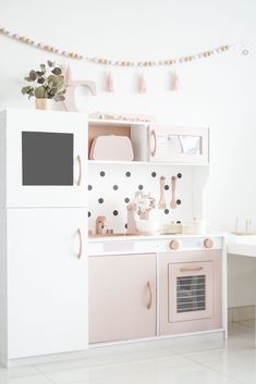 a white and pink kitchen with polka dot wallpaper on the walls, potted plant next to the stove