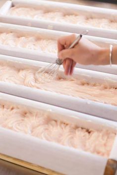 a person whisk icing on top of a cake in a box with white frosting