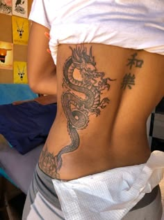 a woman with a dragon tattoo on her lower back is standing in front of a bed