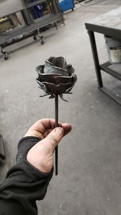 a person holding up a metal flower in their left hand, with other tools behind them