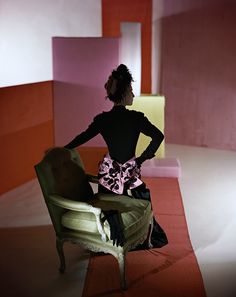 a woman sitting in a chair with her back to the camera, looking at an abstract painting