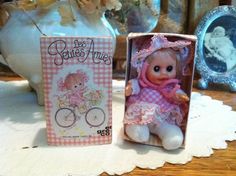 a small doll in a pink dress next to a box with an image of a baby on it