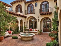 a courtyard with couches and a fountain in front of a house that has many windows