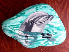 a painted rock with a dolphin swimming in the water on top of a wooden table