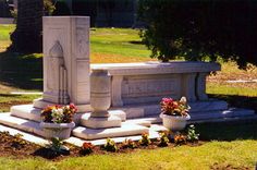 the monument is surrounded by flowers and potted plants in front of it, along with two urns on either side