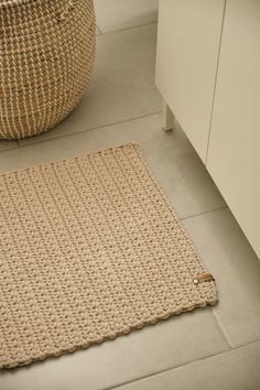 a crocheted rug sits on the floor in front of a basket and cabinet