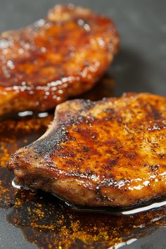 two pieces of meat sitting on top of a pan covered in oil and seasoning