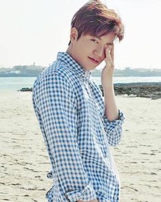 a young man standing on top of a sandy beach next to the ocean with his hand near his face