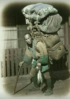 an old black and white photo of a man carrying bags on his back while walking