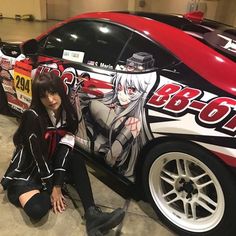 a woman sitting on the ground next to a car painted with anime characters and graphics