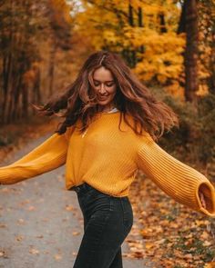 a woman in yellow sweater and black pants skateboarding down a path with leaves on the ground