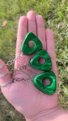 a hand holding three pieces of green plastic in it's palm, with chains attached to them