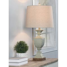 a table lamp sitting on top of a wooden table next to a book and potted plant