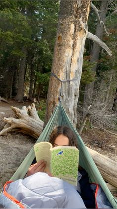 a woman laying in a hammock reading a book with a tree behind her