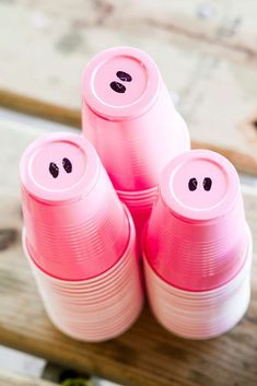 four pink cups with faces on them sitting on a wooden table next to other items