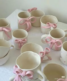 a table topped with lots of white cups and saucers covered in pink bowknots