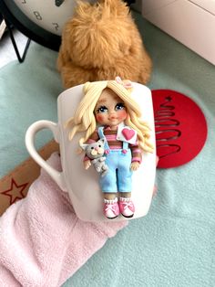 there is a coffee cup with a doll on it next to a teddy bear and other items