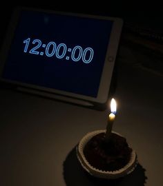 a lit candle sitting on top of a cupcake in front of a tablet computer