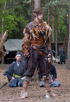 a man dressed up in costume standing next to a tree with other people around him