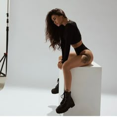 a woman sitting on top of a white block in front of a photo studio backdrop