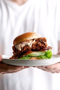 a person holding a white plate with a sandwich on top of it and lettuce