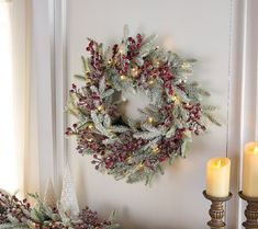 a christmas wreath and two candles on a mantle