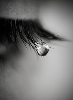 a drop of water hanging from the side of a persons eye, in black and white