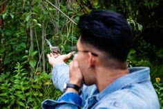 a man holding a bird up to his face while standing in front of some trees